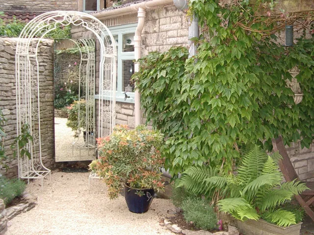 An Italianate courtyard garden, designed by Capability Charlotte. Features a wrought iron arch and a large mirror to make the space feel lighter and larger.