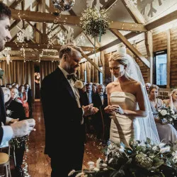 A bride and groom stand in front of a table covered in greenery