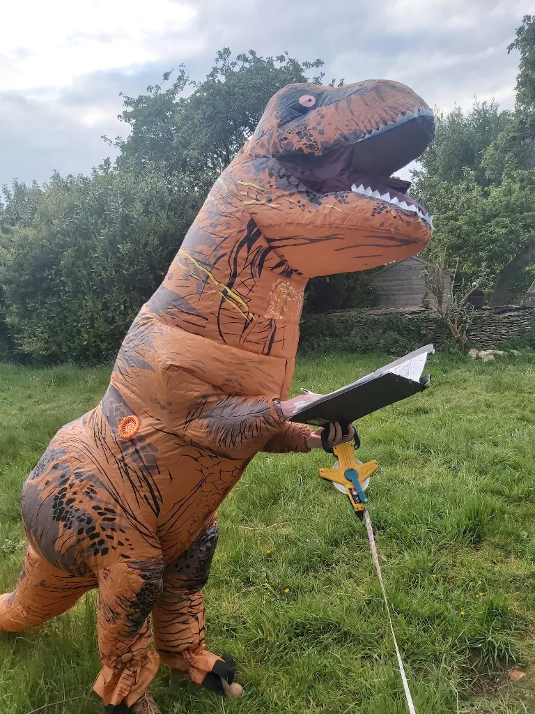 A man in a dinosaur costume holding a tape measure and clipboard