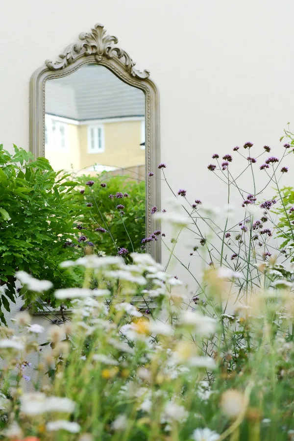 Photo by Victoria Tapper A rococco-style mirror is seen hanging on a wall through a border of wildflowers. Photo by Victoria Tapper