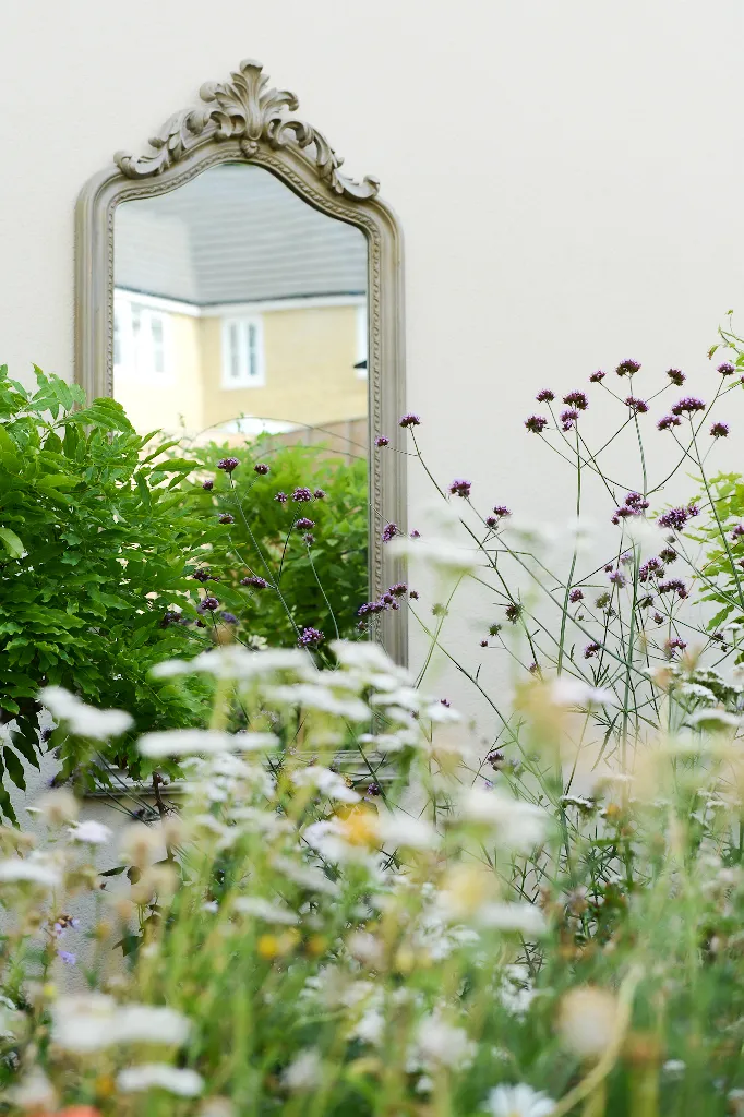 A rococco-style mirror is seen hanging on a wall through a border of wildflowers. Photo by Victoria Tapper